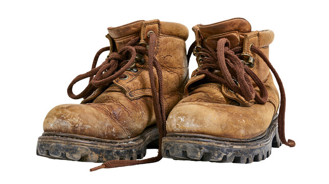 Isolated well-worn brown leather hiking boots with dirty soles and untied shoelaces.
