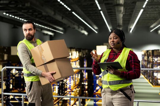 African American female staff member uses a headset to handle package tracking, cargo status and customer complaints, transmitting parcel updates for e-commerce customer service and delivery support.