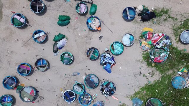 Top down aerial drone footage of traditional Vietnamese thung chai basket boats densely clustered on the sandy beach in Mui Ne. Blue round fishing boats with green nets in Binh Thuan Province Vietnam
