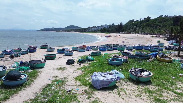Wide aerial drone view of dozens of traditional Vietnamese round basket boats scattered across the sandy shore of Mui Ne. Classic thung chai fishing boats near the waterline in Binh Thuan Vietnam.
