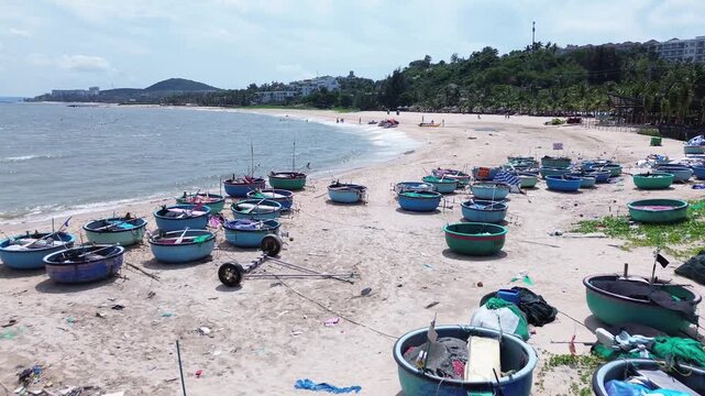 Wide aerial drone view of dozens of traditional Vietnamese round basket boats scattered across the sandy shore of Mui Ne. Classic thung chai fishing boats near the waterline in Binh Thuan Vietnam.