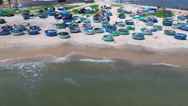 Wide aerial drone view of dozens of traditional Vietnamese round basket boats scattered across the sandy shore of Mui Ne. Classic thung chai fishing boats near the waterline in Binh Thuan Vietnam.