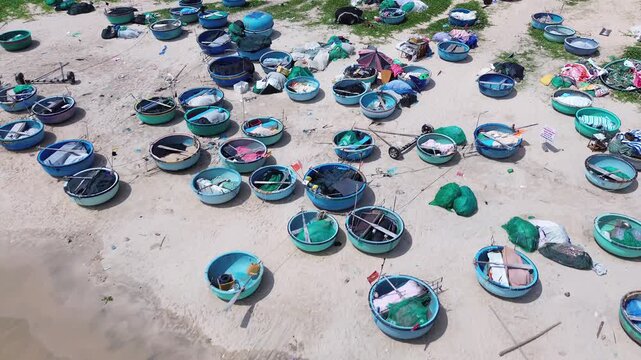 Wide aerial drone view of dozens of traditional Vietnamese round basket boats scattered across the sandy shore of Mui Ne. Classic thung chai fishing boats near the waterline in Binh Thuan Vietnam.