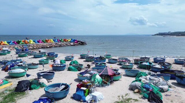 Aerial drone shot of traditional blue thung chai fishing boats on Mui Ne beach next to colorful X-shaped wave breakers. Vibrant coastal landmark scene with sea in Binh Thuan Province Vietnam.