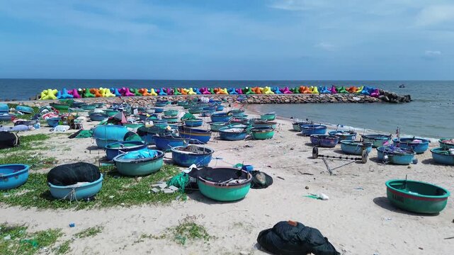 Aerial drone shot of traditional blue thung chai fishing boats on Mui Ne beach next to colorful X-shaped wave breakers. Vibrant coastal landmark scene with sea in Binh Thuan Province Vietnam.