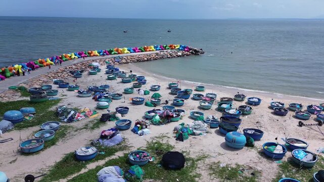 Aerial drone shot of traditional blue thung chai fishing boats on Mui Ne beach next to colorful X-shaped wave breakers. Vibrant coastal landmark scene with sea in Binh Thuan Province Vietnam.
