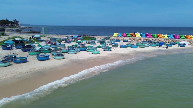 Low angle aerial view of traditional Vietnamese basket boats resting on sand and grass in Mui Ne. Colorful X-shaped wave breakers along the shoreline with sea in Background in Binh Thuan Vietnam.