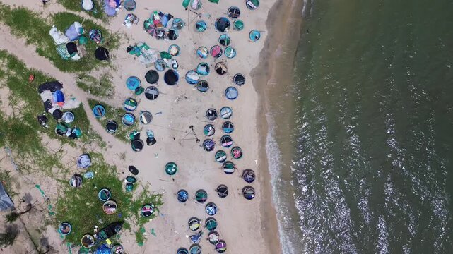 Top down aerial drone perspective capturing geometric pattern of blue round traditional Vietnamese coracle fishing basket boats parked on sandy beach shore in Mui Ne bay near Phan Thiet.