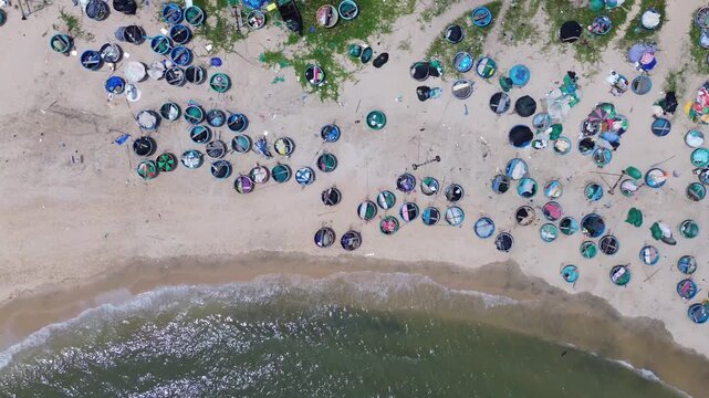 Top down aerial drone perspective capturing geometric pattern of blue round traditional Vietnamese coracle fishing basket boats parked on sandy beach shore in Mui Ne bay near Phan Thiet.