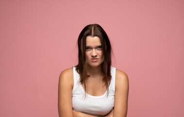 Obraz premium Young woman standing with arms crossed, grumbling on a pink background, expressing irritation and displeasure