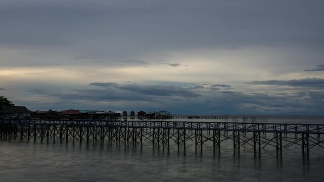 Time lapse at Mabul Island shows a long wooden jetty and stilt village as heavy cloud cover softens the sunset and the scene fades into blue hour.