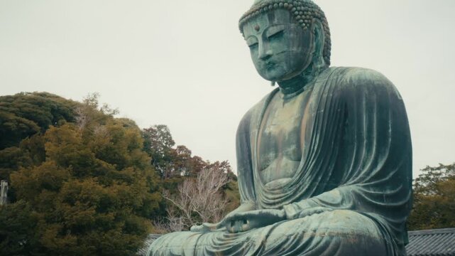 The monumental bronze Great Buddha of Kamakura, housed at Kotoku-in Temple in Japan, displays its iconic weathered green patina and tranquil expression against a backdrop of autumn trees.