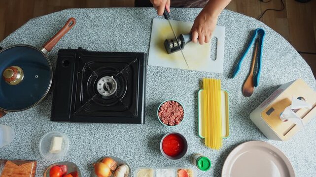 Top view of person sharpening chef knife on cutting board surrounded by pasta ingredients
