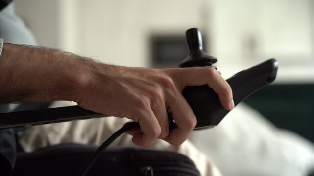 Disabled man's hand controlling electric wheelchair joystick