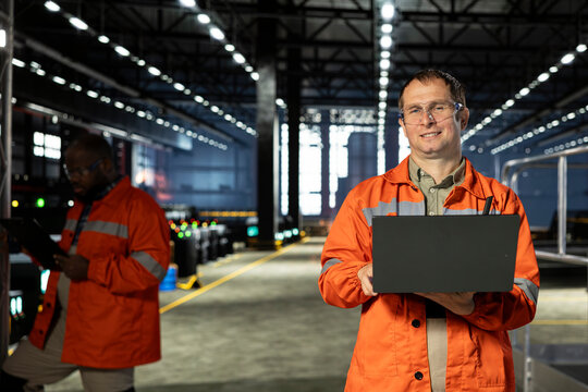 Industrial employee inspects steel equipment with a laptop on the factory floor, wearing safety glasses while supporting engineering, metal manufacturing and heavy-industry production operations.