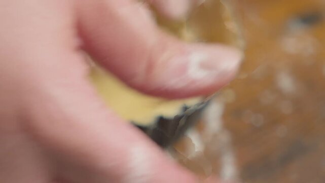 Pastry chef rolling out dough for tartlets on a floured wooden work surface, with several tart molds prepared for baking. Close-up of traditional pastry preparation in a bakery kitchen.