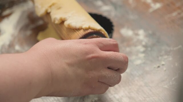 Pastry chef rolling out dough for tartlets on a floured wooden work surface, with several tart molds prepared for baking. Close-up of traditional pastry preparation in a bakery kitchen.