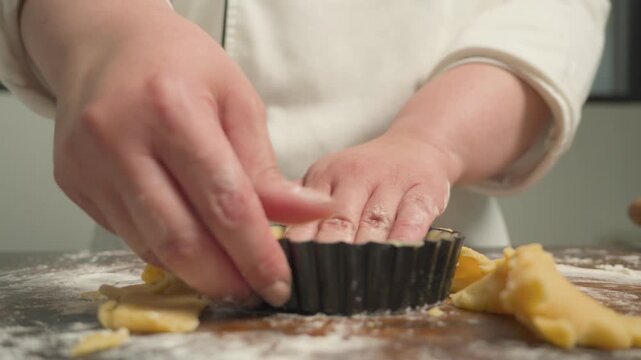 Pastry chef rolling out dough for tartlets on a floured wooden work surface, with several tart molds prepared for baking. Close-up of traditional pastry preparation in a bakery kitchen.