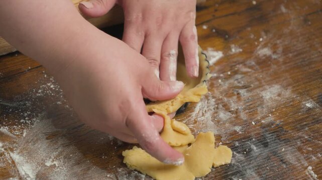 Pastry chef rolling out dough for tartlets on a floured wooden work surface, with several tart molds prepared for baking. Close-up of traditional pastry preparation in a bakery kitchen.