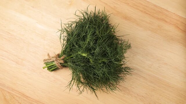 Fresh dill bunch rotating on a wooden board