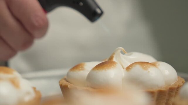 Close-up of a lemon tart topped with toasted meringue being caramelized with a kitchen blowtorch, showcasing the golden-brown meringue and crisp pastry crust. Cinematic food preparation shot with shal