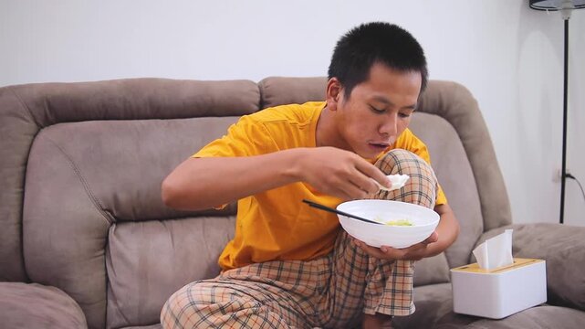 Young man eating noodles and crackers on cozy sofa