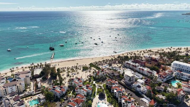 Aerial drone view of a long white sand beach with palm trees, thatched umbrellas and boats on the turquoise water, Punta Cana, Dominican Republic