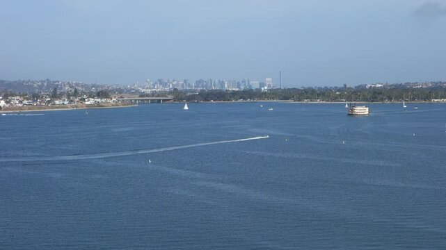 Fast moving boat over a calm blue Mission Bay water under a clear sky with a distant San Diego city skyline, Southern California