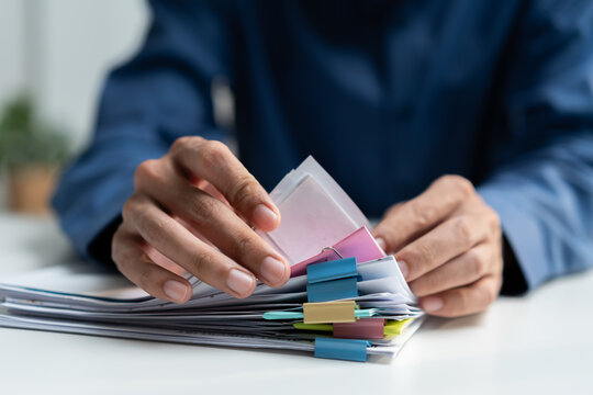 Businessman organizing paperwork and files with colorful clips at an office desk, representing document management, administration, filing, records, organization, and corporate workflow.