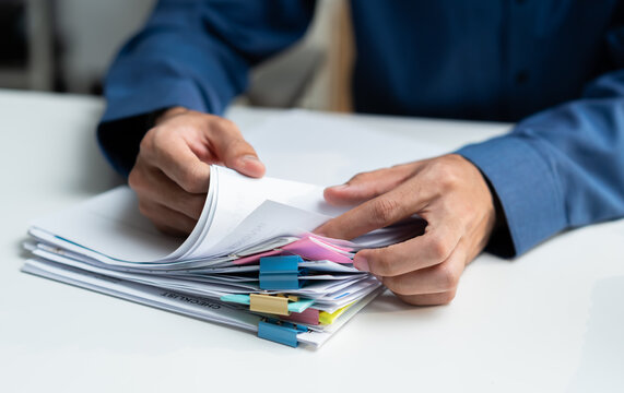 Close-up of professional businessman hands searching financial document files with colorful sticky notes at office desk. Male employee organizing corporate paperwork and business audit concept.