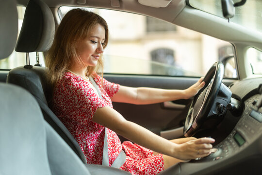 Positive young adult woman driving car during solo trip, side view