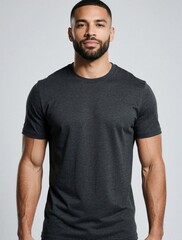 Fototapeta premium Athletic man with beard wears dark heather gray t shirt, poses in studio. Male model stands against plain light gray background, showing upper body, short sleeve shirt apparel.