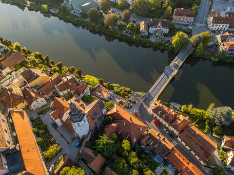 Aerial top-down view of the parish church, historic red-roofed buildings, and road bridge across the Mur River in Frohnleiten, Styria, Austria