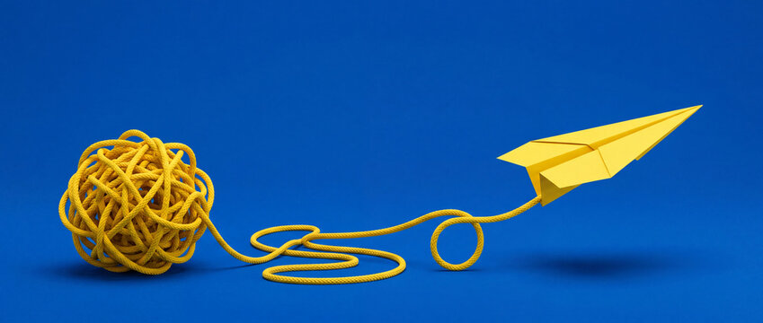 Yellow paper plane emerging from a tangled rope ball on blue background, symbolizing creative solutions, innovation, and simplifying complex business problems.