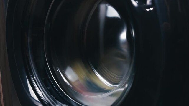 Washing machine drum rapidly spinning, generating dynamic reflections and motion blur on its dark, curved surface, symbolizing efficiency, hygiene, and the ongoing cycle of daily chores