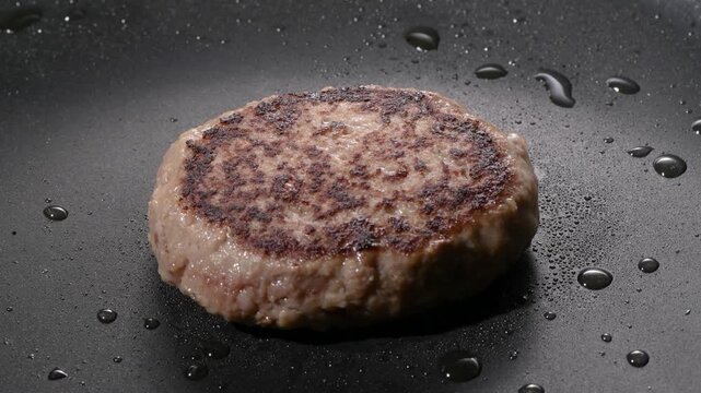 Grilled hamburger steak patty with seared crust cooking on a black griddle, camera zooms in and pans across the surface