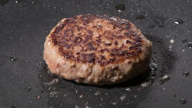 Grilled hamburger steak patty with seared crust cooking on a black griddle, camera zooms in and pans across the surface
