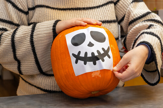 Young woman applying skeleton face template to Halloween pumpkin