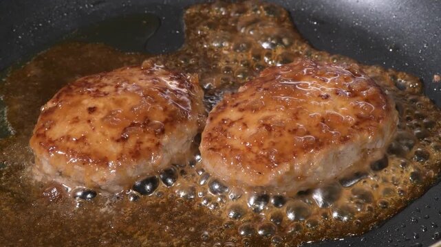 Two raw hamburger steak patties starting to cook on a black frying pan before browning