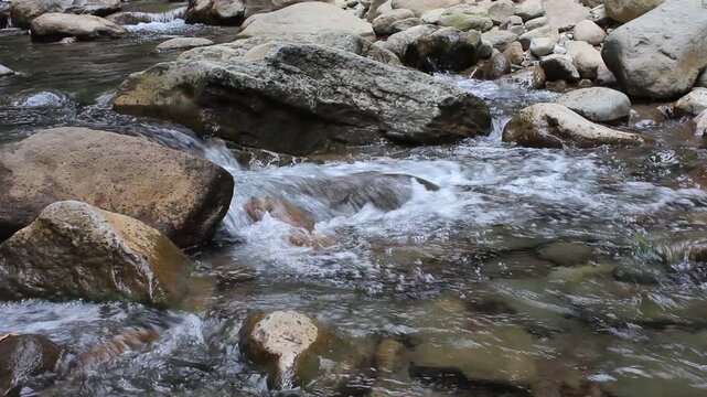Relaxing river water gently flowing over a natural rocky streambed in a peaceful mountain environment surrounded by greenery.