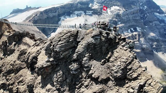 Scenic footage of the Peak Walk suspension bridge connecting two mountain peaks at Glacier 3000 in the Swiss Alps, with visitors crossing the high-altitude bridge surrounded by dramatic alpine scenery