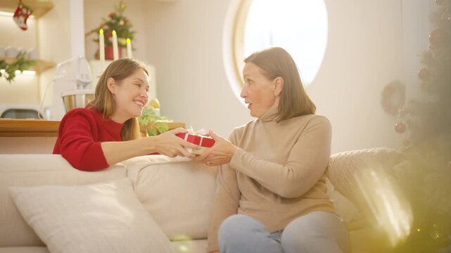 Family Christmas festive holiday celebration. Adult daughter giving gift to senior mother at home. Happy Caucasian women sharing special moment bonding with family and seasonal tradition celebrating