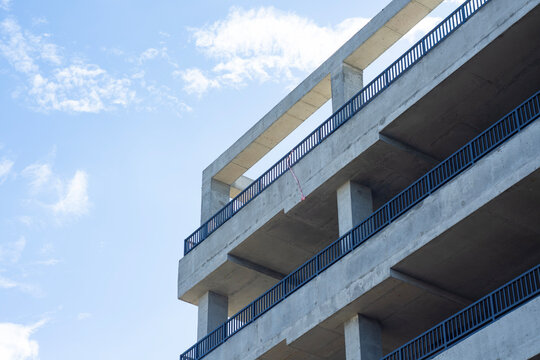 Modern reinforced concrete multi level parking garage structure under construction against blue sky. Urban development, architectural engineering and commercial real estate building concept.