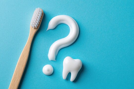 White toothpaste forms question mark shape on blue background next to wooden toothbrush. Dental care concept with tooth shaped paste. Oral hygiene, dental health questions for patients, dentists.