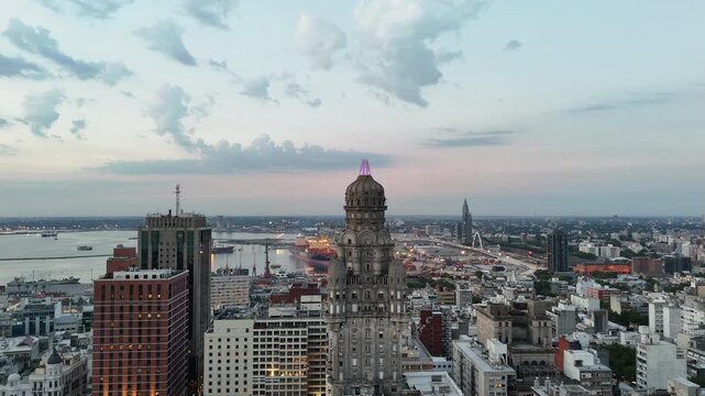 Arial view of Palacio Salvo and Plaza Independencia in Montevideo, Uruguay, with the harbor, city buildings and pastel sky at twilight.
