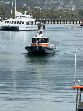 SANTA BARBARA, CA, APR 9, 2026: Harbor Patrol response boat motoring through the harbor channel, leaving a wake, with a catamaran yacht and pier behind
