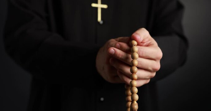 Priest in cassock with rosary on black background, closeup