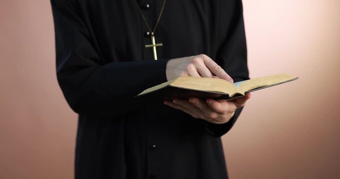 Priest in cassock reading Holy Bible on pale brown background, closeup