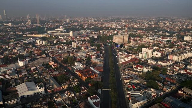 Panoramic aerial drone shot of Esteban de Antuniano boulevard transitioning into 31 Poniente avenue in Puebla with light traffic under hazy sunset sky and distant city skyline background