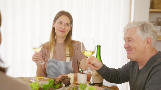 Senior parents and adult daughter enjoy Christmas dinner together at home. Happy family sharing festive holiday meal with roast chicken, salad and wine around dining table during seasonal celebration.